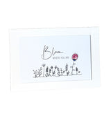 A square white greeting card with a white border, featuring the words 'Bloom WHERE YOU ARE' in black script and serif text above a simple line drawing of wildflowers. A small pink flower illustration with a blue stem and yellow center is on the right side.