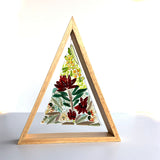 A triangular wooden frame containing a fused glass triangle depicting Australian native blooms such as Waratah, Bottlebrush and Golden Wattle.