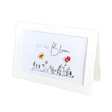 A white square greeting card with a black line drawing of wildflowers and the words 'BUZZ AND Bloom'. Two small flower-shaped pins, one yellow with a black center and one red with a black center, are attached to the card, which is photographed on a clean white background.