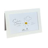 A white greeting card with a textured border, featuring a hand-drawn style illustration of a sun with the words 'shine BRIGHT' and small flower drawings at the bottom.